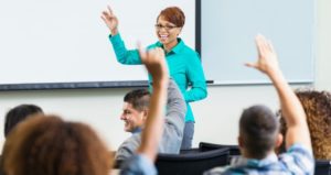 Professor smiling, students hands raised