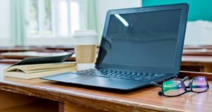 Laptop and books on desk of classroom.