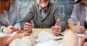 teacher talks with students around table with thumbs up