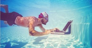 Man swimming underwater also checks his email on his laptop in the pool