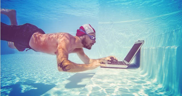 Man swimming underwater also checks his email on his laptop in the pool