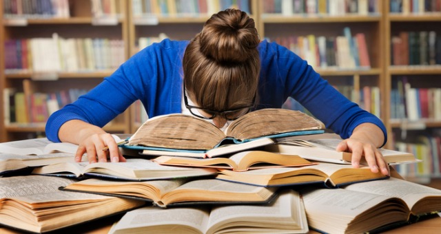 Student surrounded by books and feeling overwhelmed