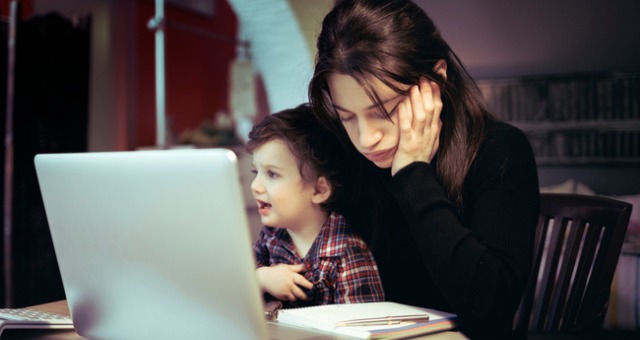 Student mom sits at computer with antsy child