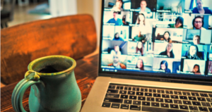 Zoom meeting occurs on computer screen with coffee mug on table next to laptop