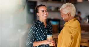 Two people laugh with one another while chatting and drinking coffee