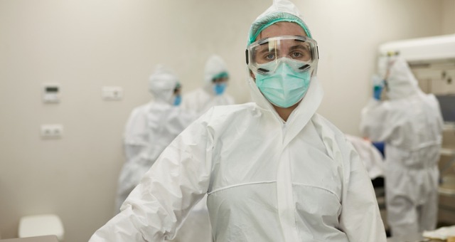 Healthcare worker wears gear and masks while looking exhausted