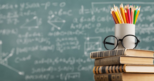 Chalkboard in background with books, glasses and pencils sitting in front of it