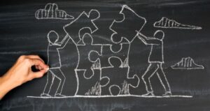 Drawing on chalkboard depicts people working together to complete puzzle pieces