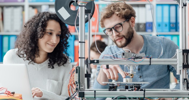 Two college students work on 3D printer during lab class