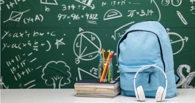 Backpack and school supplies in front of chalkboard with writing