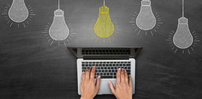 Laptop with lightbulbs above and chalkboard in back