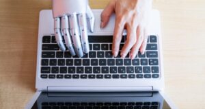 Robot hand and human hand on laptop keyboard