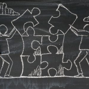 Drawing on chalkboard depicts people working together to complete puzzle pieces